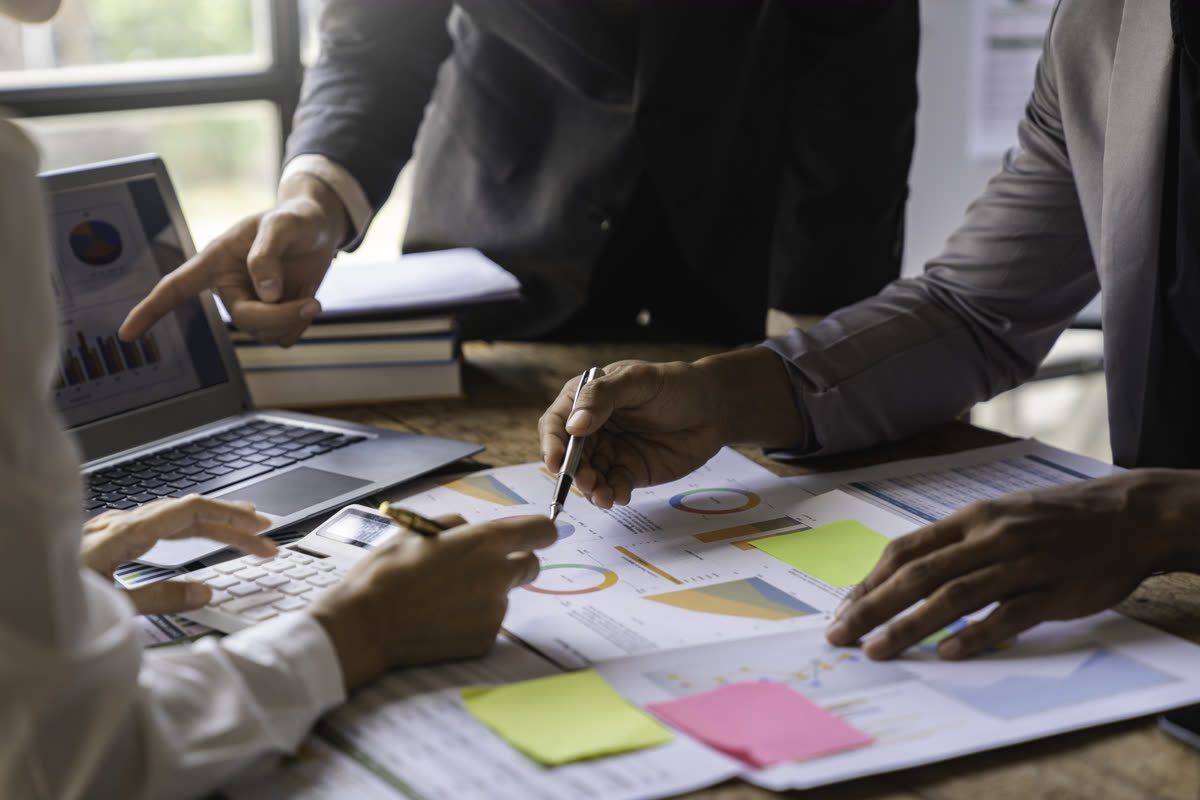 Equipo revisando gráficas e informes sobre una mesa, con computadora portátil y calculadora, durante una revisión de resultados.